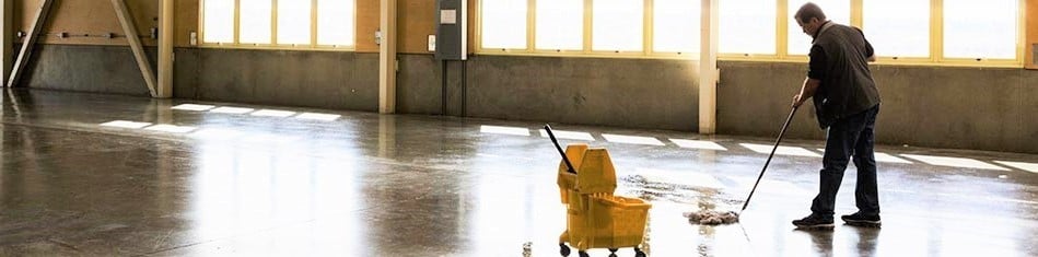 Janitor mopping the floor on a long hallway in front of a window